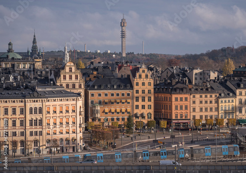 Old town Gamla Stan at the square Kornhamnstorg, skyline with tele tower Kaknästornet, blue subway passing, an autumn day in Stockholm