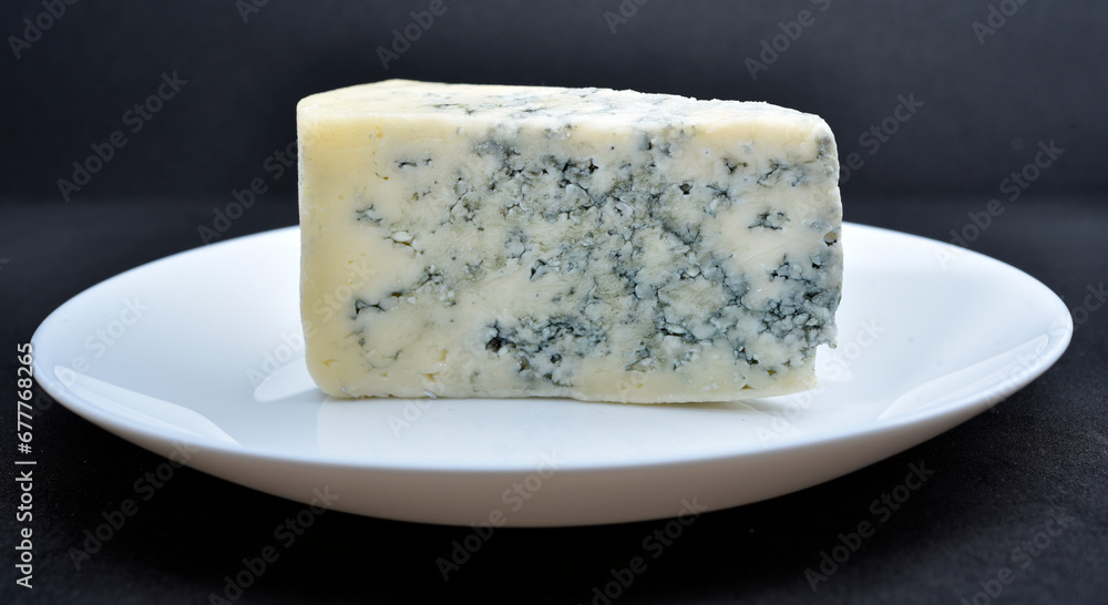 A piece of cheese with blue mold on a white plate. Delicious cheese.