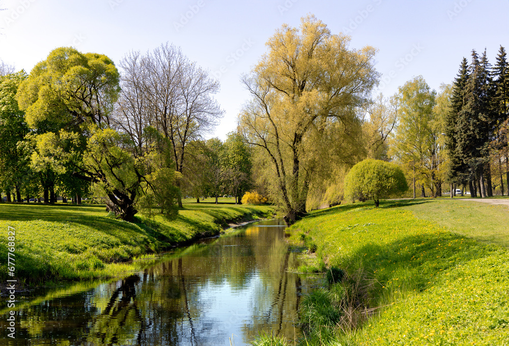 Sunny spring landscape with small pond surrounded by trees reflecting in the water in Victory Park, Riga, Latvia.