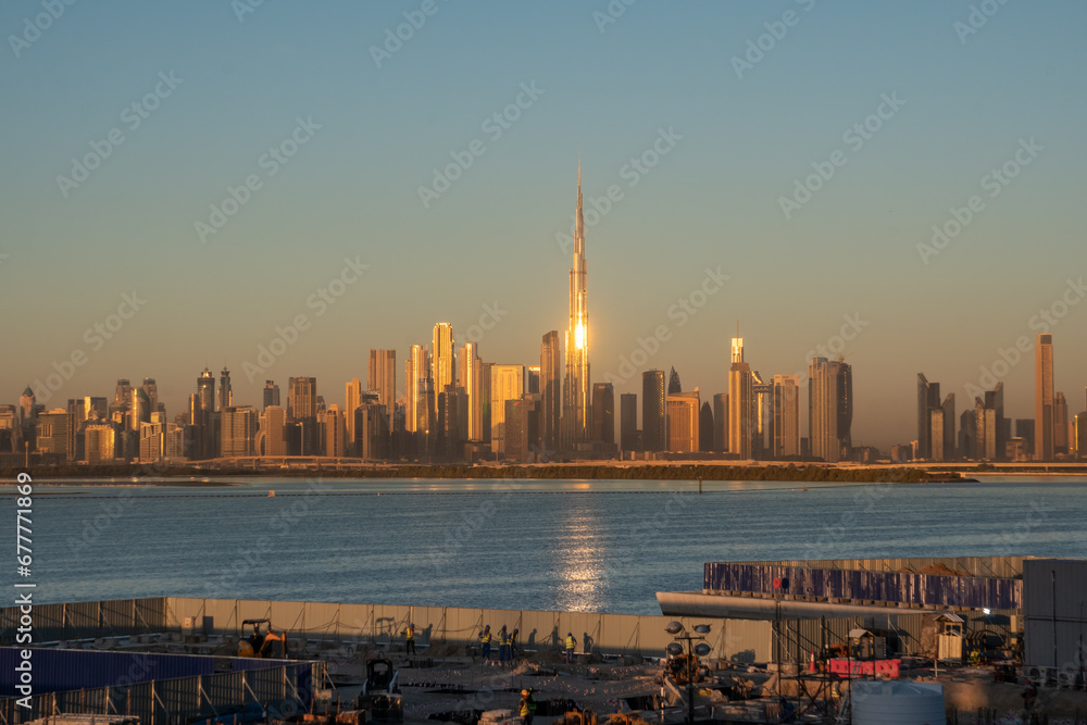 The Dubai financial district skyline with Burj Khalifa in the center point, and in the foreground the workers building the city, at sunrise
