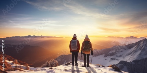 Couple man and woman hikers on top of a mountain with snow at sunset or sunrise, together enjoying their climbing success and the breathtaking view, looking towards the horizon