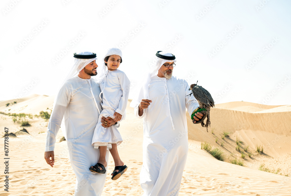 Naklejka premium Three generation family making a safari in the desert of Dubai. Grandfather, son and grandson spending time together in the nature and training their falcon bird.