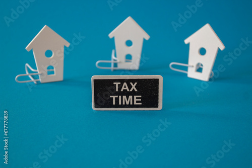 Wooden houses sits next to a wooden black board with the word Tax Time. beautiful blue background. Business  tax time concept  copy space.