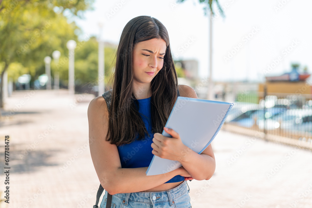 Fototapeta premium Young Brazilian student woman at outdoors with sad expression