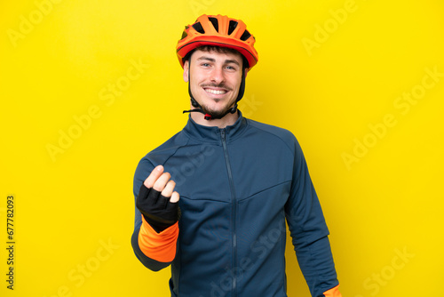 Young cyclist caucasian man isolated on yellow background making money gesture