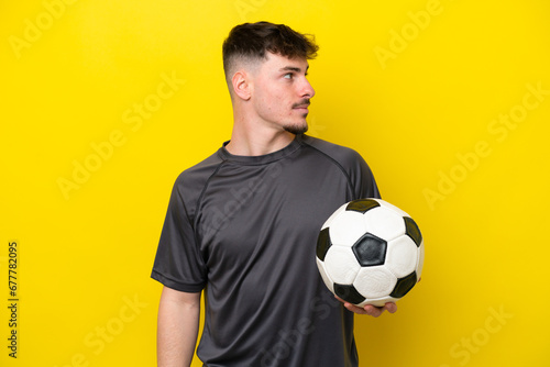 Young football player man isolated on yellow background looking to the side