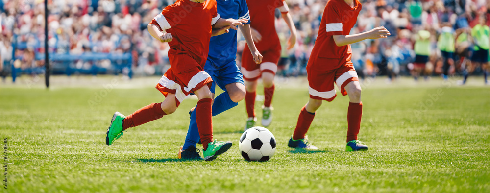 Football soccer match for children. Boys playing a football game in a school tournament. Picture of kids competition while playing a European football game at the stadium filled with spectators Football soccer match for children. Boys playing a football game in a school tournament. Picture of kids competition while playing a European football game at the stadium filled with spectators