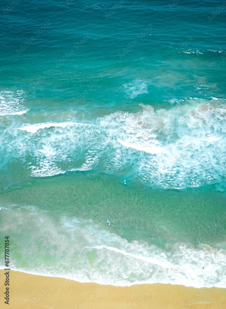 Vertical of the beautiful foamy waves of the turquoise, teal sea captured from above