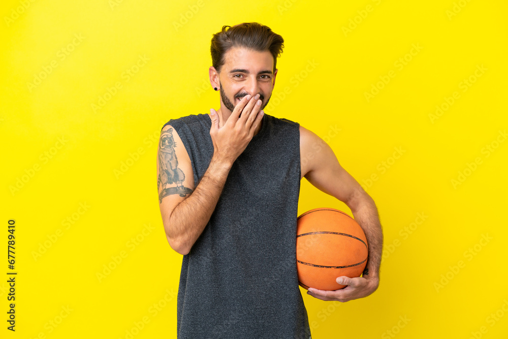 Handsome young basketball player man isolated on yellow background happy and smiling covering mouth with hand