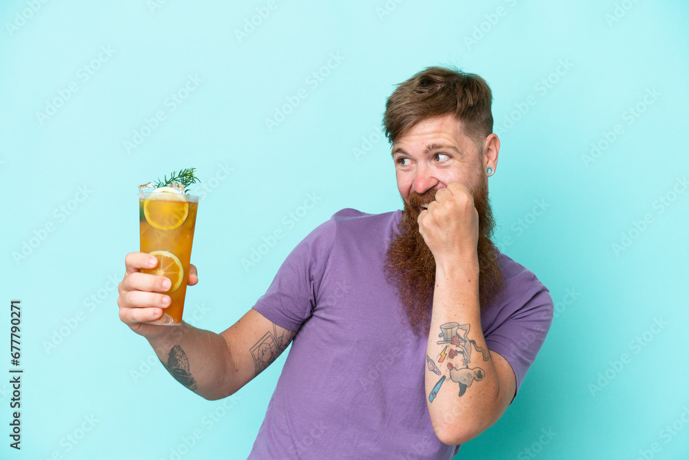 Redhead man with long beard holding a cocktail isolated on blue background celebrating a victory Redhead man with long beard holding a cocktail isolated on blue background celebrating a victory
