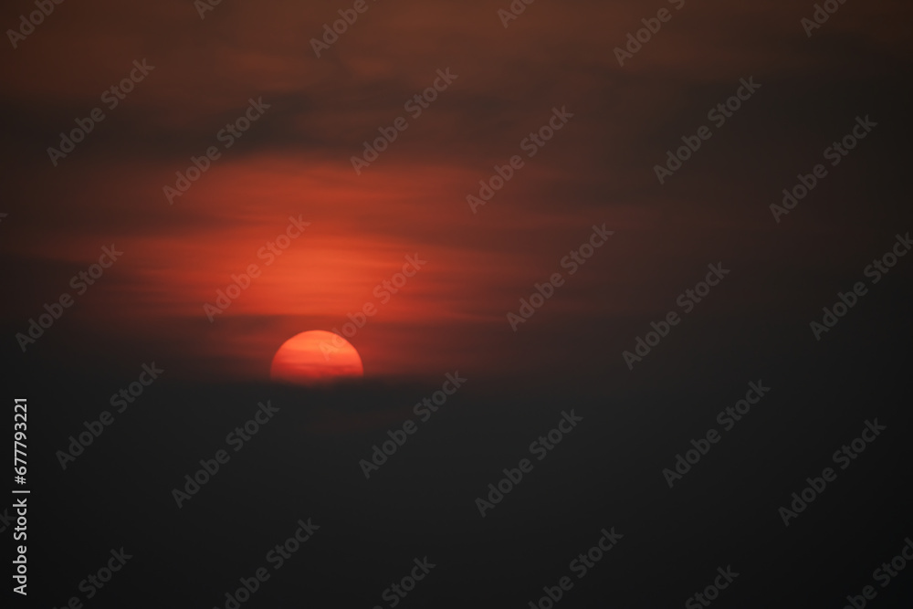 Scenic golden red sunset, half Sun hidden behind thick clouds, tropical sky, close up photo