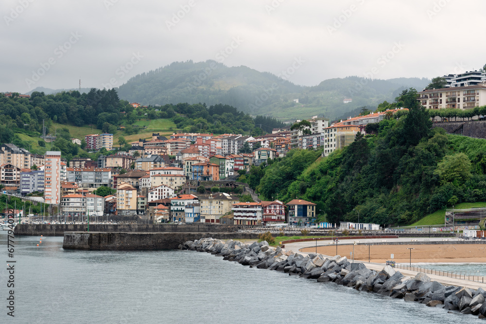 View of Mutriku village nestled in a valley between mountains under a stormy sky from the breakwater, Gipuzkoa, Basque Country, Spain, Gipuzkoa, Basque Country, Spain