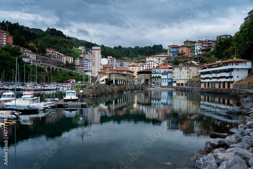 View of Mutriku village and its reflection in the harbor waters in the morning under a dramatic cloudy sky, Gipuzkoa, Basque Country, Spain