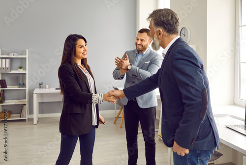 Business team showing professional recognition and work appreciation to a young female colleague. Happy young woman gets promoted and exchanges handshakes with her mature boss or senior manager