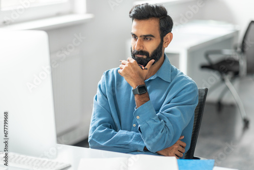 Thoughtful indian man with beard looking at computer
