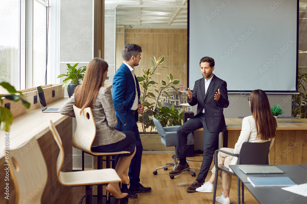 Business team having discussion during a corporate work meeting in the office. Group of young people together with their manager talking about current work projects in a modern workplace Business team having discussion during a corporate work meeting in the office. Group of young people together with their manager talking about current work projects in a modern workplace