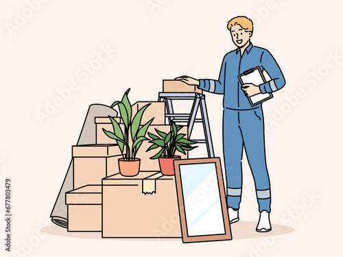 Man mover stands near pile of cardboard boxes advertising services of company that helps with moving to new home. Mover guy in blue uniform works in logistics business providing delivery services.