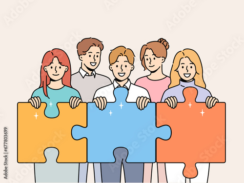 Friendly team of men and women hold giant puzzle pieces symbolizing working together to solve business problems. Business people with smile doing teamwork to increase company income