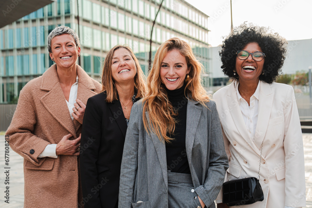 Group of proud businesswomen smiling and looking at camera at workplace. Real executive women staring front, laughing together with suit and successful expression. Corporate female employees meeting - obrazy, fototapety, plakaty 