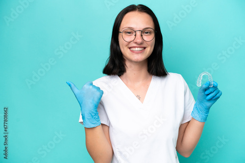 Young caucasian woman holding envisaging isolated on blue background pointing to the side to present a product
