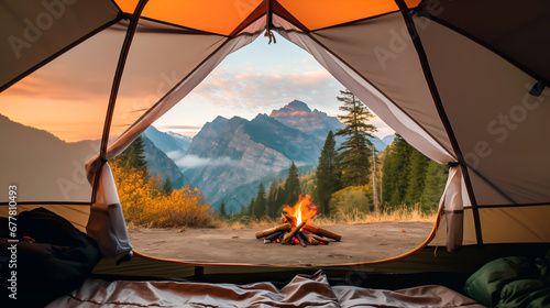 Tent view of majestic mountains at sunrise with a campfire. 
