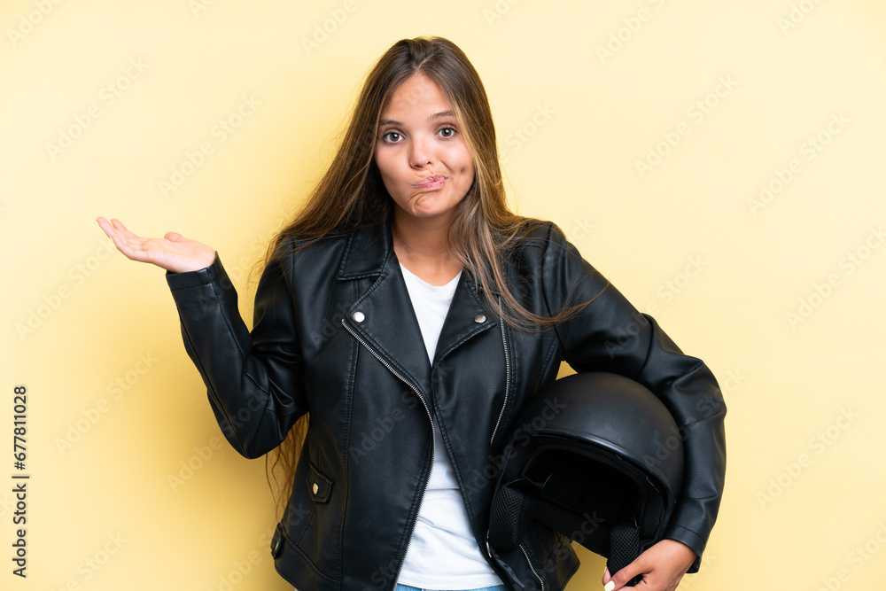 Young caucasian woman with a motorcycle helmet isolated on yellow background having doubts while raising hands Young caucasian woman with a motorcycle helmet isolated on yellow background having doubts while raising hands