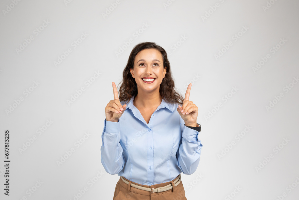Positive millennial caucasian woman in formal wear pointing fingers up at copy space Positive millennial caucasian woman in formal wear pointing fingers up at copy space