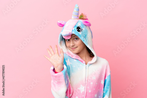 Little caucasian woman wearing a unicorn pajama isolated on pink background saluting with hand with happy expression