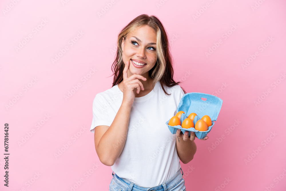 Young Russian woman holding eggs isolated on pink background thinking an idea while looking up Young Russian woman holding eggs isolated on pink background thinking an idea while looking up