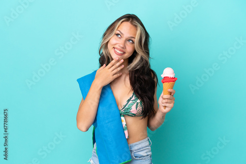 Teenager caucasian girl holding ice cream and towel isolated on blue background looking up while smiling