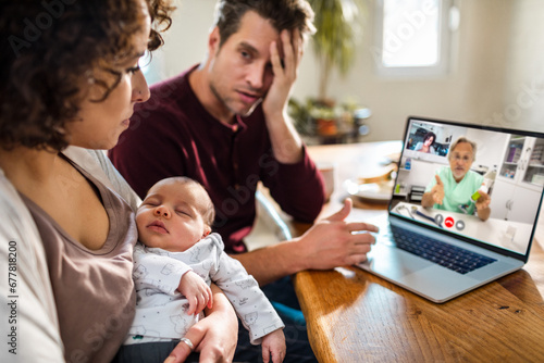 Young couple talking to their pediatrician over a video call on their laptop while holding their newborn baby photo