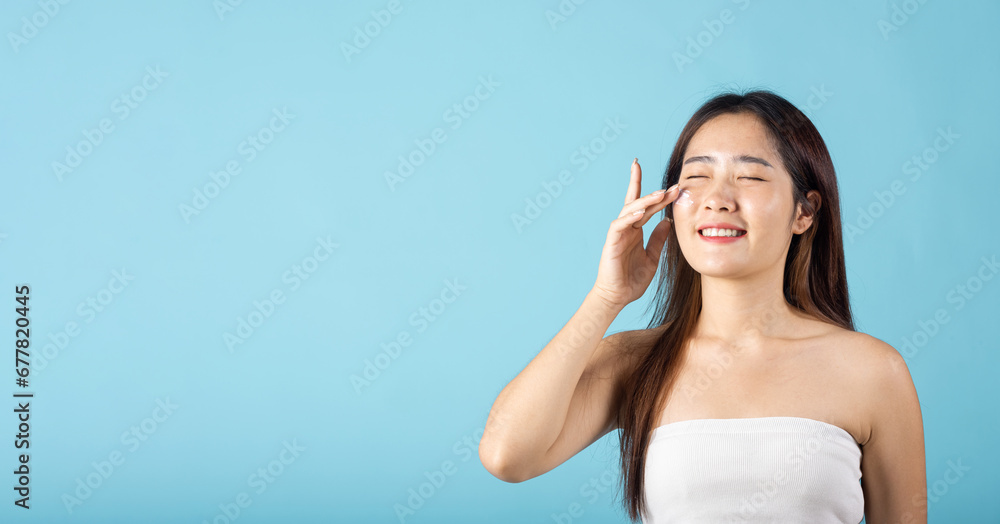 Happy beauty portrait woman gets cream on her cheek, Beautiful young female smiling applying cosmetic cream on her face isolated on blue background, health clean skin, Skin care and beauty concept Happy beauty portrait woman gets cream on her cheek, Beautiful young female smiling applying cosmetic cream on her face isolated on blue background, health clean skin, Skin care and beauty concept
