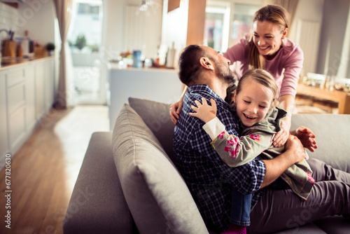 Happy family with little daughter playing at home on couch