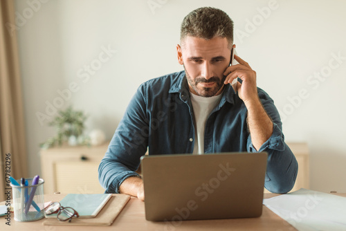 businessman answering calls on mobile phone while using laptop indoor