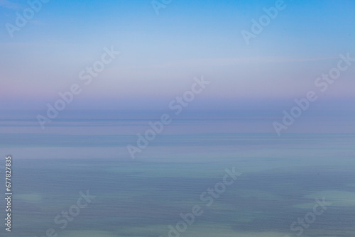 Blue sky with haze and blurry glowing pink clouds above the sea. Shallow coastal sea water with azure patterns. Ripples in the water © yegorov_nick