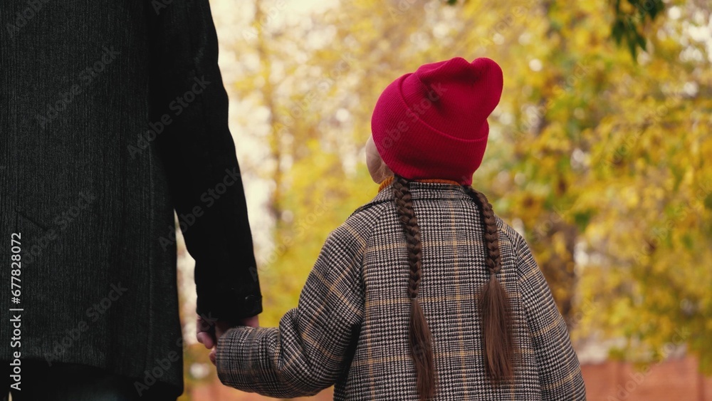 Happy little girl looks at father walking together across autumn garden