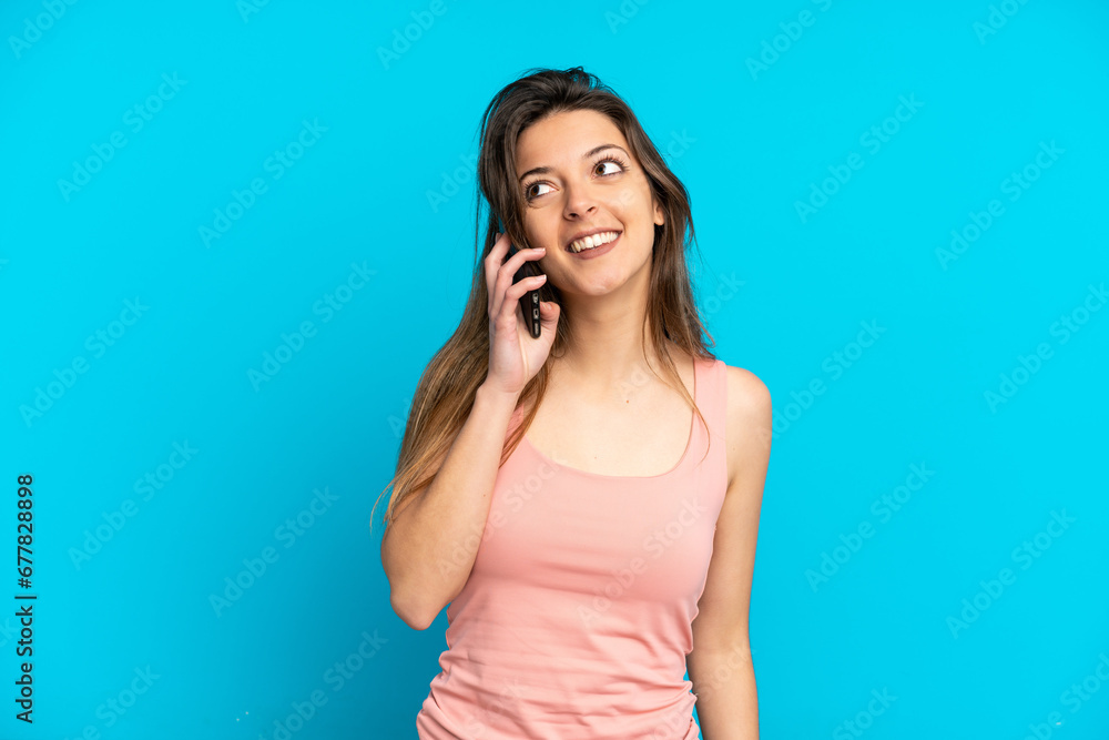 Fototapeta premium Young caucasian woman using mobile phone isolated on blue background thinking an idea while looking up