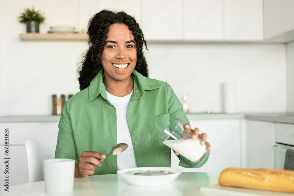african woman pouring milk into bowl with cereals in kitchen african woman pouring milk into bowl with cereals in kitchen