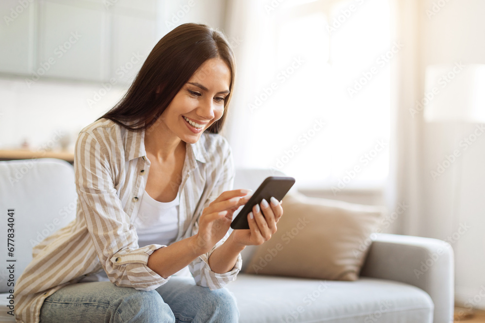 Smiling Young Woman Using Smartphone While Resting On Couch At Home Smiling Young Woman Using Smartphone While Resting On Couch At Home