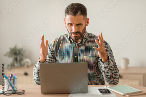 Bearded middle aged guy gesturing angry at laptop issue indoor