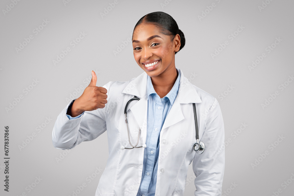 Cheerful pretty millennial black lady doctor in white coat make thumb up sign with hand Cheerful pretty millennial black lady doctor in white coat make thumb up sign with hand