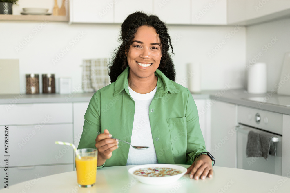 Young African American woman eating healthy breakfast at modern kitchen