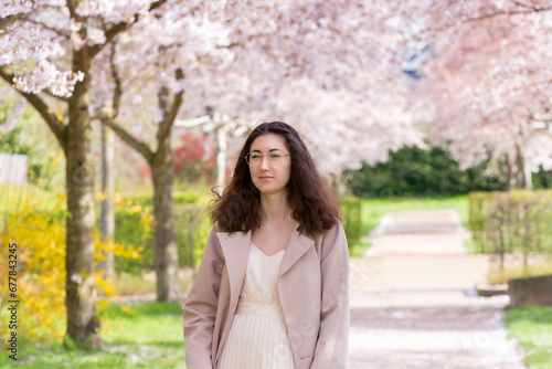 Portrait of a young girl in a beautiful dress against the background of cherry blossoms in pastel colors, who walks along the alley. Natural beauty of a woman. Spring concept.