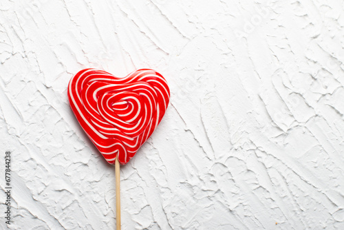 Red lollipop on a stick in the form of a heart on a white background. The concept of love and sweets. Flat layout, top view, copy space. Valentine's card. 14 of February