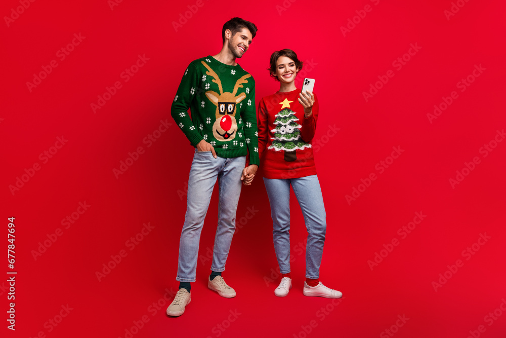 Full length portrait of positive lovely partners hold hands use smart phone isolated on vivid red color background Full length portrait of positive lovely partners hold hands use smart phone isolated on vivid red color background