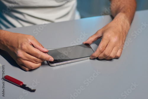 glass tempered protection film replace change mobile service. man hand uses wet wipes cloth to remove dust from black smartphone screen. new protector tempered glass top view white table.