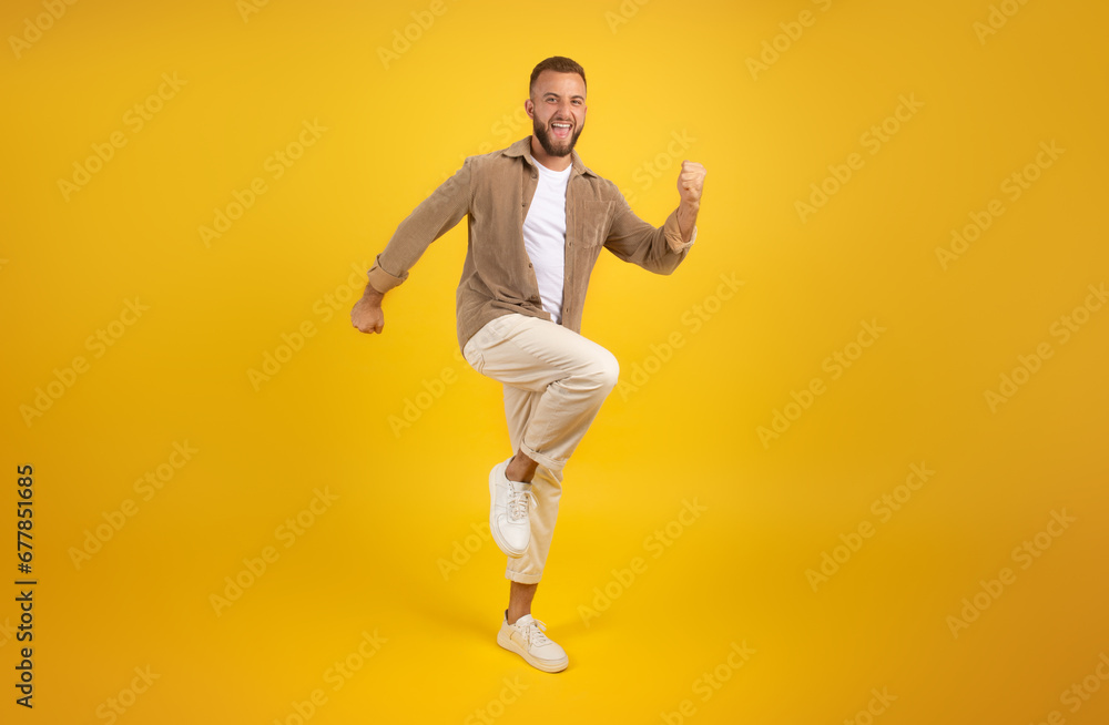 Cheerful young caucasian guy with beard in casual has fun, dance, jumping, freezes in air