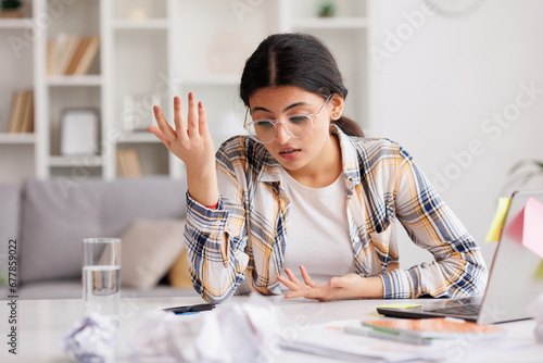 A tired young Indian girl gets angry from the number of tasks, crumples up the paper and throws it away, tries to calm down by meditating. Stressful work and study, overtasking. photo