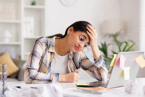 A tired young Indian girl gets angry from the number of tasks, crumples up the paper and throws it away, tries to calm down by meditating. Stressful work and study, overtasking, headache.