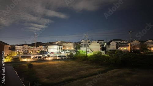 Time lapse pan over suburban houses by busy road at night as clouds move overhead photo